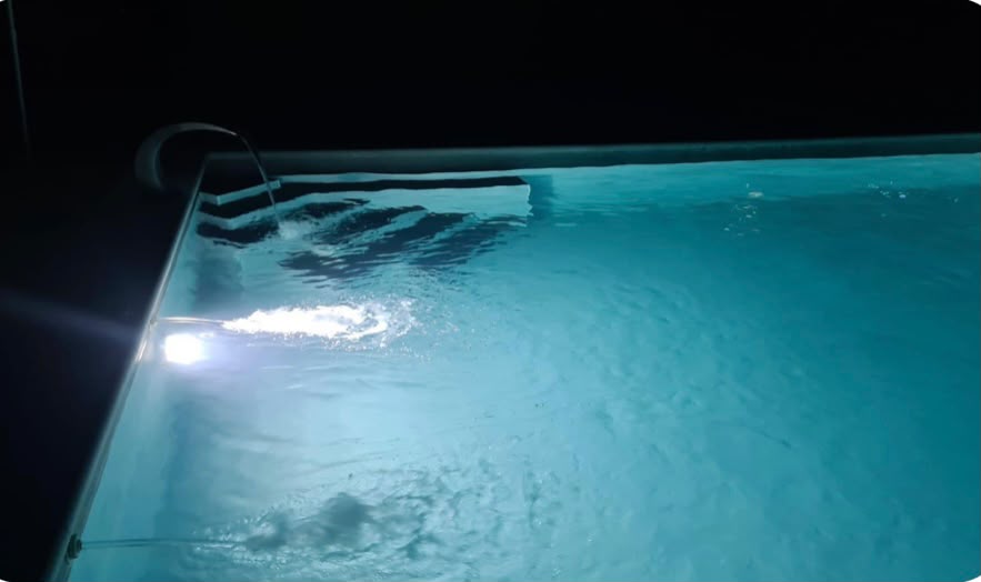 Detalle de la piscina con cascada y luz nocturna